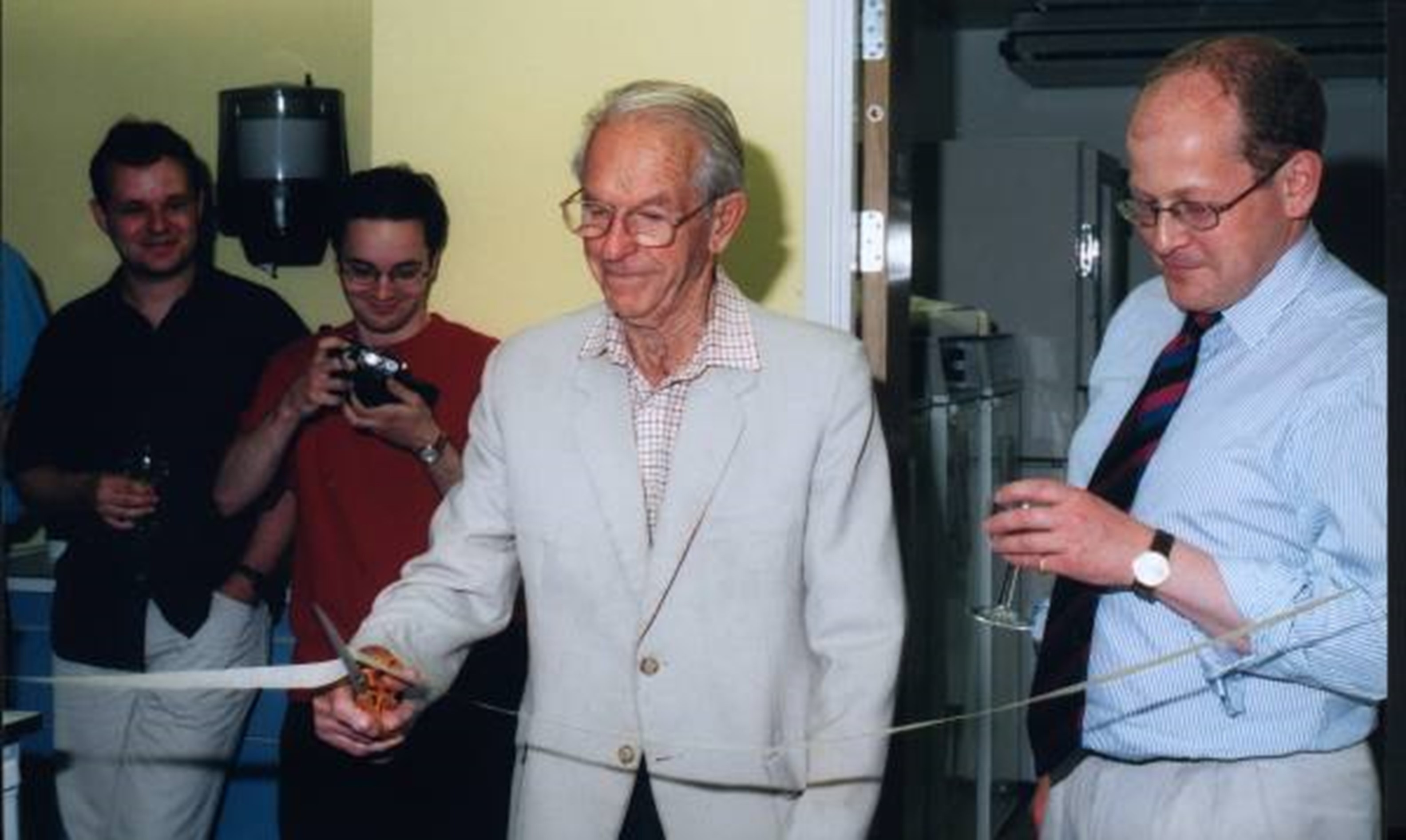 Fred Sanger ceremonially cuts a strip of autoclave tape, to declare refurbished lab space open.